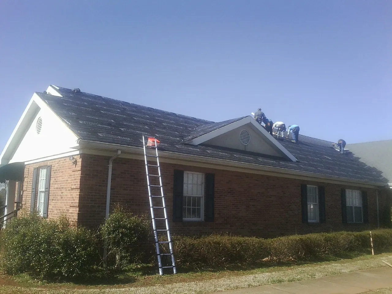 Crew tearing shingles off a brick ranch roof with a ladder set — Metal Roof Repair work by our crew in East Brookfield