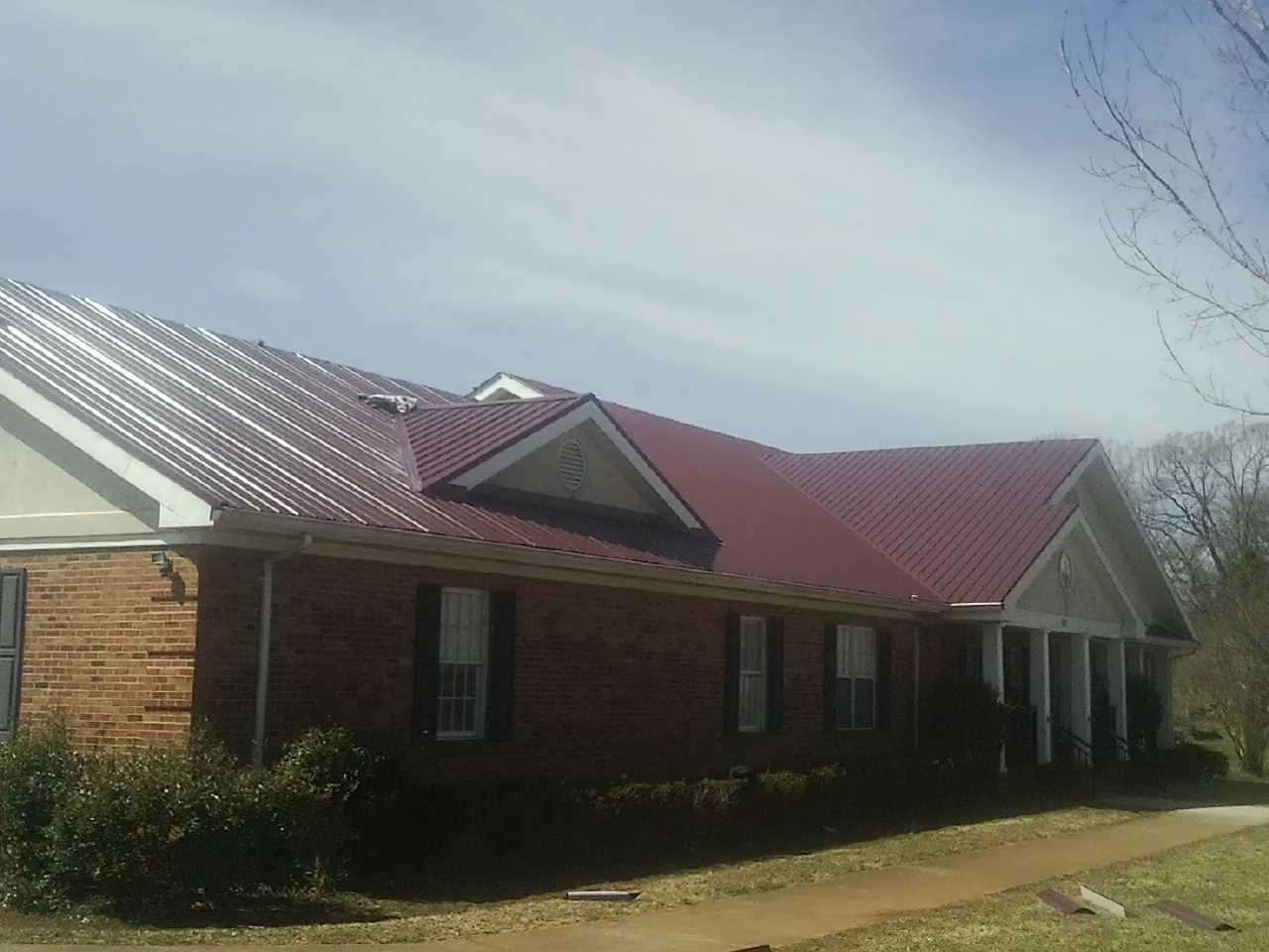 Red metal roof with gabled entries on a long brick building, from a Hail Damage Roof Repair job in East Brookfield