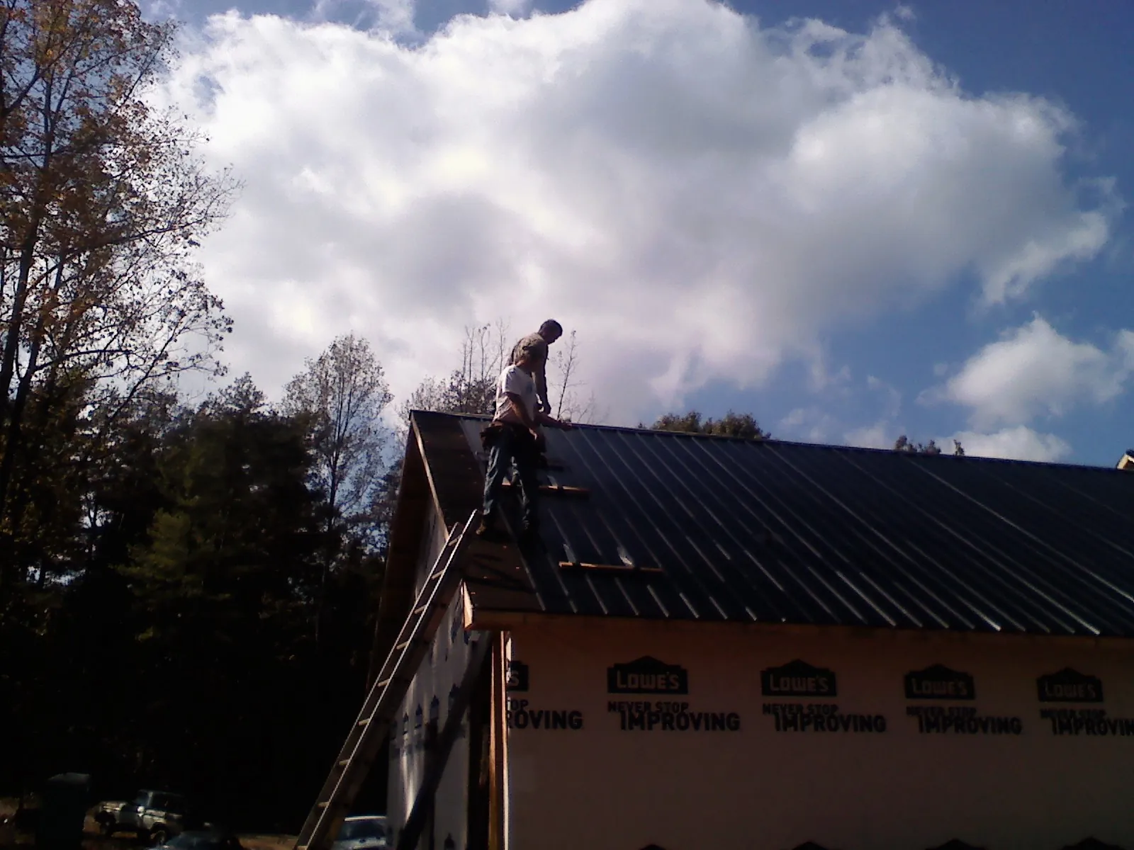 Roofer fastening dark metal panels high against a cloudy sky, from a Roof Inspection job in East Brookfield