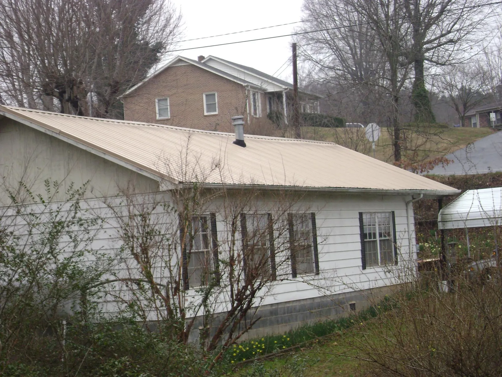 Tan metal roof on a white sided house set into a hillside — Commercial Roofing by Roofing Brothers in East Brookfield